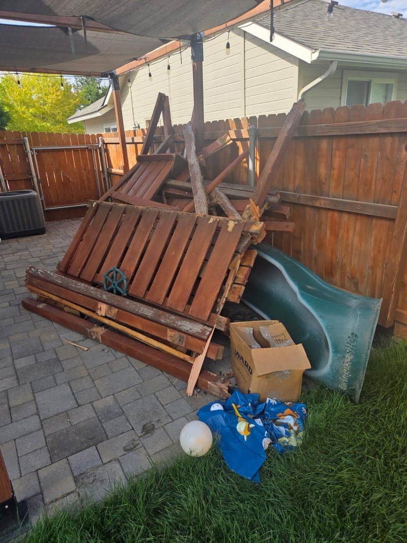 Dismantled wooden play structure, slide and pergola lumber piled on a backyard paver patio before HaulWorks removal in Meridian, Idaho